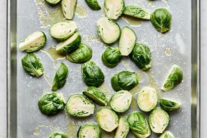 raw Brussels sprouts cut in half tossed in olive oil and salt on a baking sheet ready to be roasted in the oven