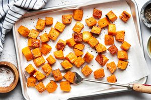 cubed roasted butternut squash seasoned with olive oil, salt and pepper on a baking sheet with a serving fork
