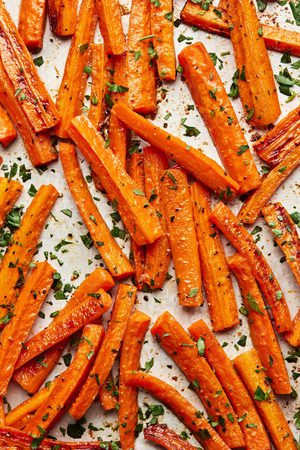 roasted carrots with caramelized edges on a baking sheet seasoned with salt, pepper and garlic powder sprinkled with parsley