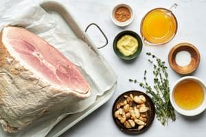 a ham, Roasted garlic, honey, orange juice, dijon, fresh thyme, cinnamon and salt in bowls on the counter