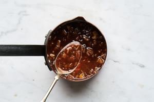 homemade honey-sweetened, herb-and-orange glaze in a small sauce pan with a spoon for roasted garlic honey baked ham