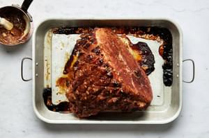 a baked homemade roasted garlic honey baked ham in a roasting pan with a honey-sweetened, herb-and-orange glaze