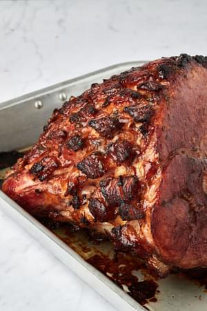 a baked homemade roasted garlic honey baked ham in a roasting pan with a honey-sweetened, herb-and-orange glaze