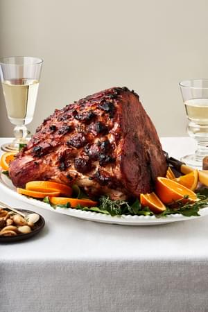 a homemade roasted garlic honey baked ham on a serving platter surrounded by bay leaves and fresh orange slices