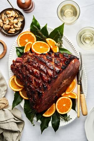 a homemade roasted garlic honey baked ham on a serving platter surrounded by bay leaves and fresh orange slices