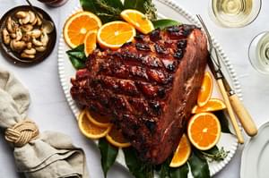 a homemade roasted garlic honey baked ham on a serving platter surrounded by bay leaves and fresh orange slices