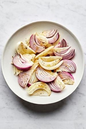 raw onion wedges tossed with olive oil, red wine vinegar, lemon juice, dijon, spices and brown sugar ready for roasting