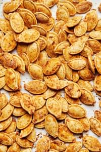 roasted pumpkins seeds on parchment seasoned with salt, garlic powder, onion powder, paprika, mustard powder and pepper