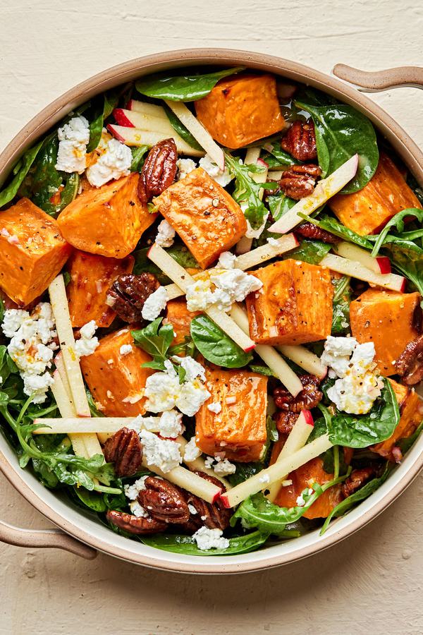 Roasted Sweet Potato Salad with Orange Vinaigrette in a serving bowl made with arugula, spinach, goat cheese and apples