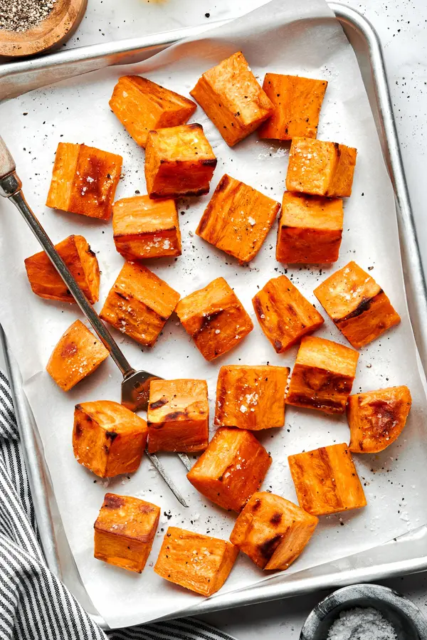roasted sweet potatoes seasoned with olive oil, garlic powder, salt & pepper on a parchment lined baking sheet