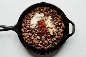 browned ground beef, chili powder, onion powder and garlic powder being cooked together in a skillet