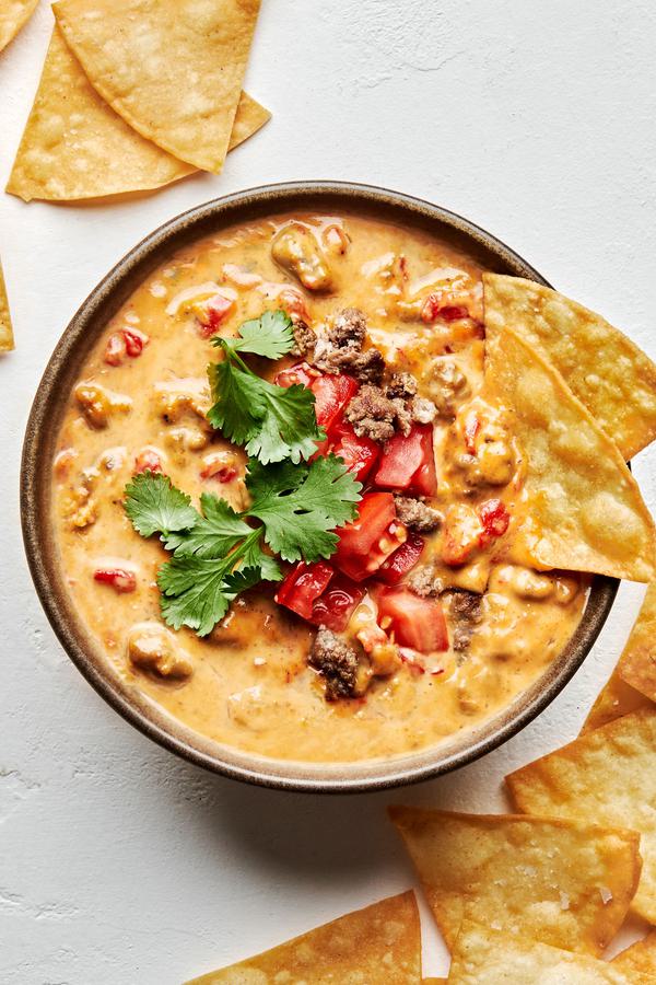 a bowl of rotel dip topped with cilantro and tomatoes served with tortilla chips