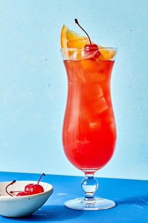 large glass of rum punch topped with an orange slice and a maraschino cherry.
