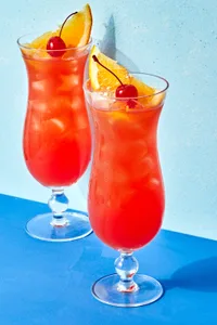 Rum punch in two tall glasses topped with cherries and a slice of orange.
