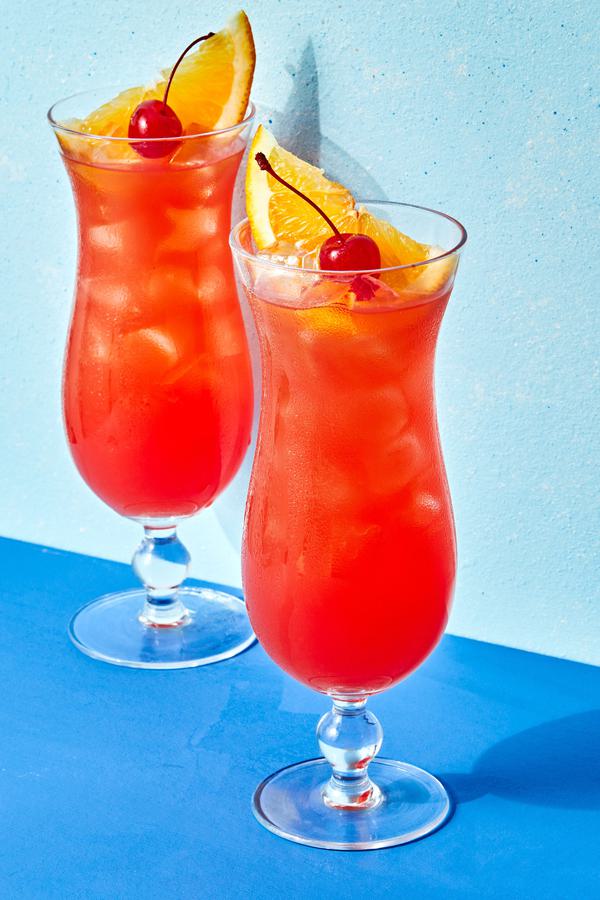 Rum punch in two tall glasses topped with cherries and a slice of orange.
