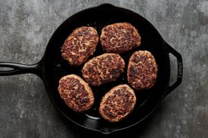 Salisbury steaks sizzling in a pan, developing a perfectly browned crust as they cook to golden, juicy perfection.