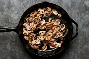 onions, garlic and mushrooms being cooked in a cast iron skillet