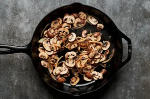 onions, garlic and mushrooms being cooked in a cast iron skillet