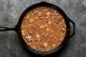 Salisbury steak gravy simmering with tender mushrooms and caramelized onions, creating a rich, savory sauce in the pan.