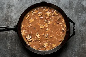 Salisbury steak gravy simmering with tender mushrooms and caramelized onions, creating a rich, savory sauce in the pan.