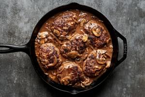 Perfectly seared Salisbury steaks in a cast iron skillet, drizzled with rich, glossy gravy for a comforting, hearty meal.