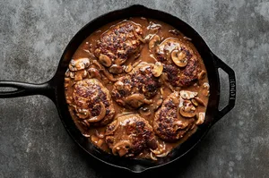 Perfectly seared Salisbury steaks in a cast iron skillet, drizzled with rich, glossy gravy for a comforting, hearty meal.