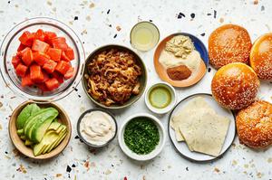 salmon, avocado, caramelized onions, mayo, buns, dill havarti cheese, and spices in bowls on the counter for salmon burgers