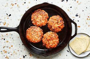 homemade salmon burger patties being fried in a skillet next to a plate of sliced dill havarti cheese