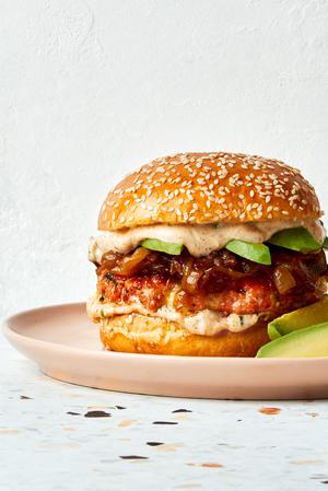 a salmon burger with old bay seasoning and topped with dill havarti cheese, caramelized onions and sliced avocado on a plate