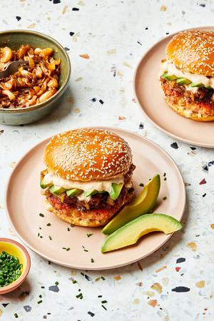 2 plates with salmon burger with old bay seasoning and topped with dill havarti cheese, caramelized onions and sliced avocado