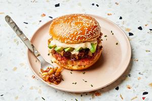 a salmon burger with old bay seasoning and topped with dill havarti cheese, caramelized onions and sliced avocado on a plate