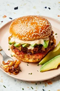 a salmon burger with old bay seasoning and topped with dill havarti cheese, caramelized onions and sliced avocado on a plate