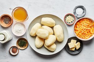 potatoes, butter, garlic, flour, chicken stock, thyme, salt, pepper, nutmeg, milk and cheese in bowls for scalloped potatoes