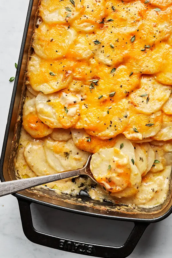 homemade scalloped potatoes covered in melted cheese in a casserole dish being scooped out with a spoon