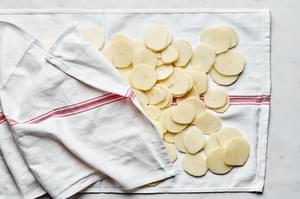 peeled, sliced and rinsed potatoes being patted dry on a kitchen towel