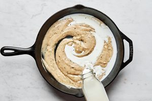 milk being poured into a skillet with butter, flour and garlic that have been cooked and thickened