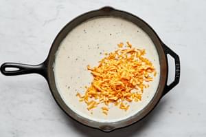 shredded cheese being added into a skillet with sauce for scalloped potatoes