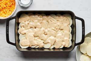 sliced potatoes and sauce layered in a greased casserole dish to make scalloped potatoes