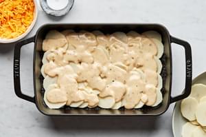sliced potatoes and sauce layered in a greased casserole dish to make scalloped potatoes