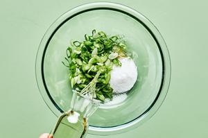 seasoned rice vinegar being poured over sugar, salt, sesame oil and green onions to make salad dressing for cucumber salad
