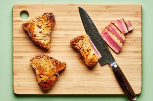 seared ahi tuna on a cutting board being sliced against the grain into 1/2 inch slices