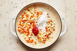 flour being added to a skillet with onions, carrots, fennel, salt and garlic that have been cooked in olive oil