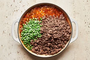 a savory filling for shepherd's pie being cooked in a skillet with beef, peas, vegetables, tomato paste and spices