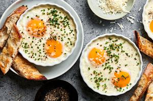 2 ramekins of shirred eggs garnished with chopped chives and served with crusty bread
