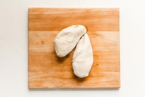 2 cooked chicken breasts on a cutting board that were boiled in water with salt