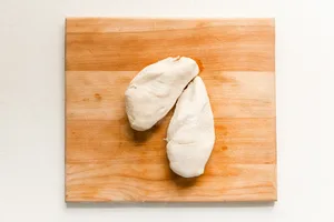 2 cooked chicken breasts on a cutting board that were boiled in water with salt