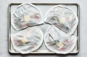 4 sealed parchment pouches full of shrimp scampi on a baking sheet ready for the oven