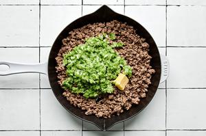 chopped bell pepper, jalapeno, onion and garlic being added to ground beef in a skillet
