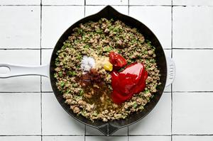 ketchup, tomato paste, spices and Worcestershire being added to a skillet with ground beef and chopped veggies