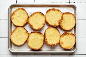 buttered, toasted hamburger buns on a baking sheet